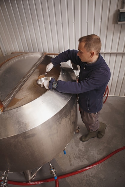 Foto de vista superior vertical de um trabalhador de uma cervejaria verificando a fermentação da cerveja em um barril