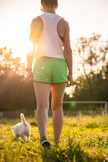 Foto de vista traseira de mulher apta em roupas esportivas, caminhando ao longo de um campo de esporte. Treino de fitness em um pôr do sol.