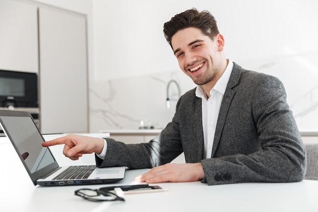 Foto de dedo acusador de hombre de negocios feliz en la pantalla de la computadora portátil, mientras realizaba el teletrabajo desde casa