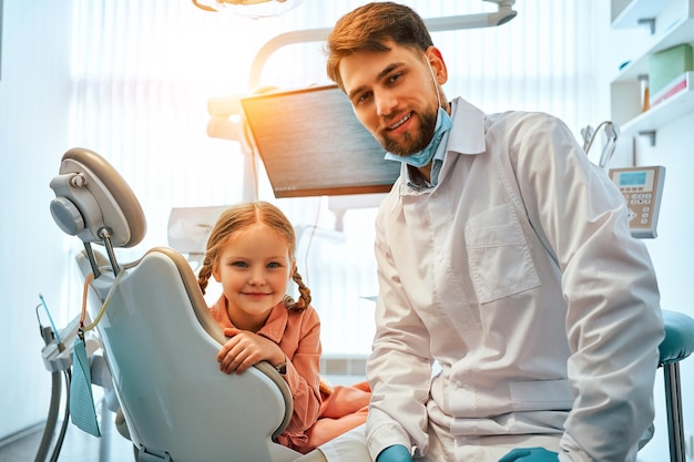 Foto de un dentista y un pequeño paciente en un sillón dental en un consultorio dental mirando a la cámara y sonriendo Medicina y cuidado dental Luz del sol