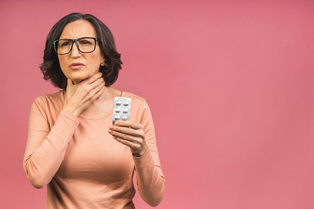 Foto der älteren reifen gealterten älteren Frau glücklich mit positivem Lächeln, das Medis-Pillen einzeln über rosafarbenem Hintergrund hält.