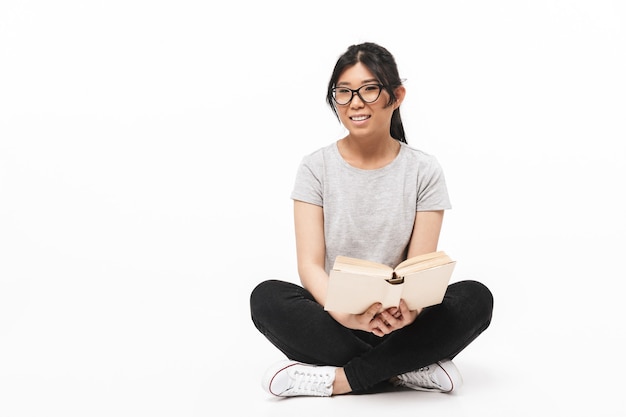 Foto der asiatischen schönen jungen Frauenaufstellung lokalisiert über der weißen Wand, die Buchlesung hält.