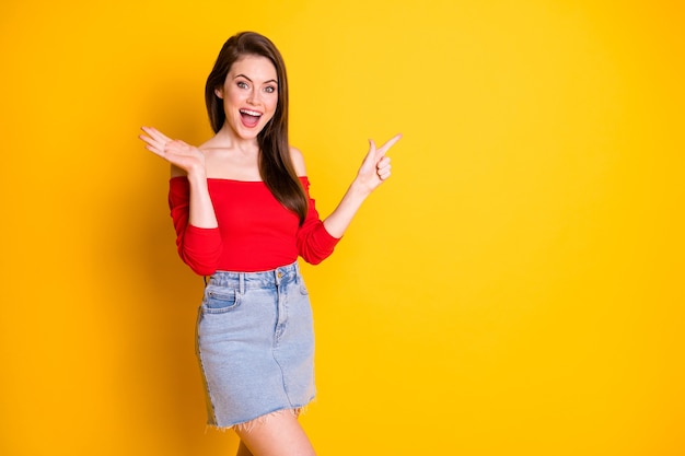 Foto der charmanten, entzückenden, aufgeregten jungen Dame, die direkt mit dem Finger leeren Raum eröffnet, bietet ein Promo-Abnutzungshemd mit unbedeckten Schultern Denim-Minirock einzeln auf leuchtend gelbem Farbhintergrund