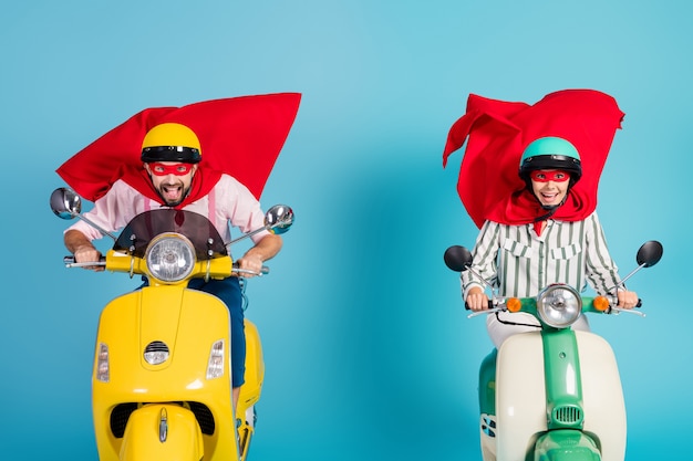 Foto der coolen Dame Kerl fahren zwei Retro Moped tragen rote Kapmaske Schutzhüte rauschen Straße Halloween Party spielen Superhelden Rollmantel fliegende Luft isoliert blaue Farbe Wand