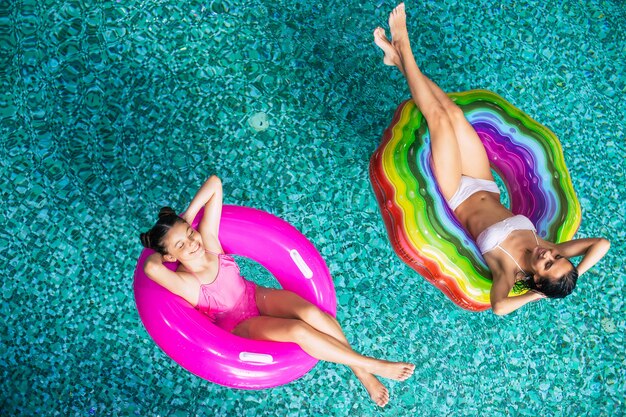 Foto der Draufsicht in voller Länge, das Sonnenbräune, glückliche Mutter und Tochter in Bikinis auf den aufblasbaren Matratzen im Schwimmbad genießt. Sommerurlaub. Entspannen im Hotelpool. Familienruhe