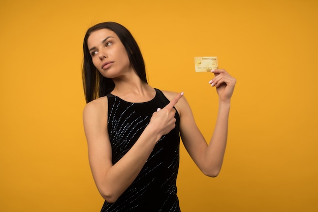 Foto der erfreuten jungen Frau, die lokalisiert über gelbem Wandhintergrund hält, der Debit- oder Kreditkarte hält.