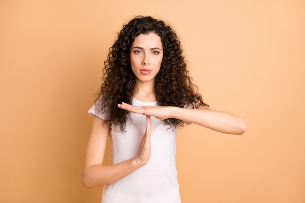 Foto der ernsten zuversichtlichen Frau, die Sie Zeitüberschreitungszeichen mit den Händen zeigt, die offen über beige Pastellfarbhintergrund starren