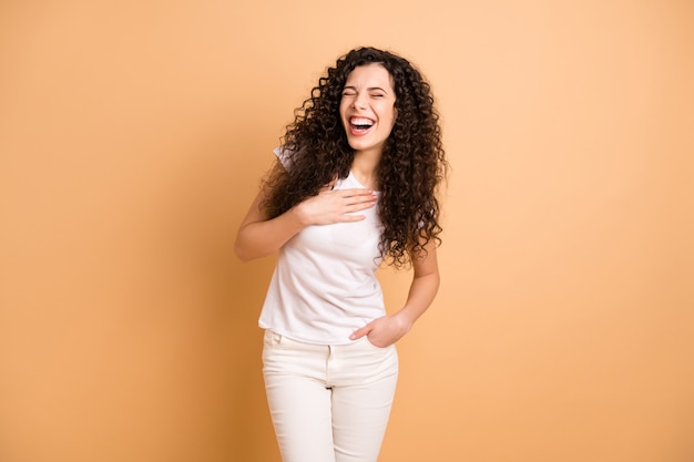 Foto der erstaunlichen Dame, die große humorvolle Geschichte hört, die Hand auf Brust hält, die laut lässig tragen weiße weiße Kleidung lokalisierte beige Pastellfarbenhintergrund lacht