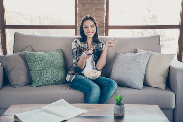 Foto der erstaunlichen Dame, die Lieblingshumorfernsehshow sieht, die Fernbedienung und Popcornplatte hält, die Sofa sitzt, lässige Kleidung Wohnung drinnen