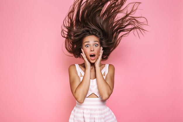 Foto der europäischen Frau 20s, die Kleid schreit und ihr langes braunes Haar schüttelt, isoliert über rosa Wand