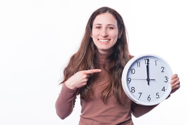 Foto der fröhlichen jungen Frau, die auf runde Uhr zeigt