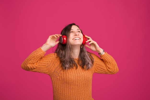 Foto der fröhlichen jungen Frau, die Musik am Kopfhörer hörend genießt, über rosa Raum stehend