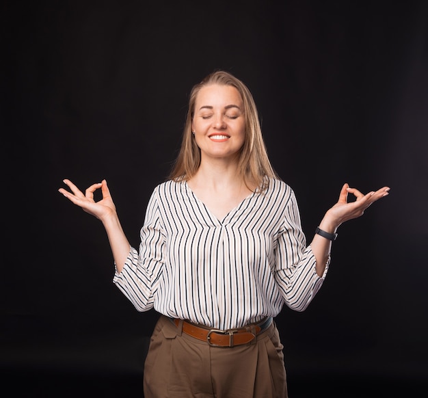 Foto der Geschäftsfrau, die Zen-Meditationsgeste auf dunklem Hintergrund macht