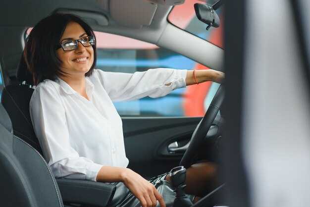 Foto der glücklichen jungen Frau, die in ihrem neuen Auto sitzt