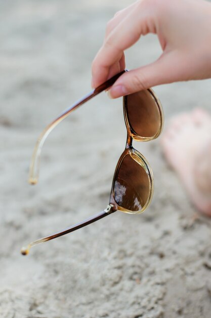 Foto der Hand der Frau, die Sonnenbrille gegen Sand hält