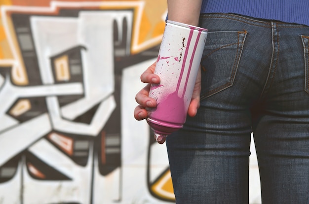 Foto der hand eines mädchens mit aerosolfarbendosen in den händen auf einem graffiti ummauern hintergrund.