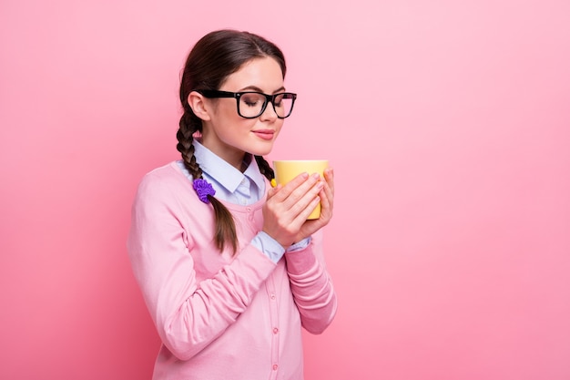 Foto der hübschen Studentin, die Hände hält, heiße, frische Getränketasse, die Augen geschlossen, einen angenehmen Geruch genießen, kleine Pause, Hausaufgaben, Hemd, Pullover, isoliert, pastellrosa Farbhintergrund