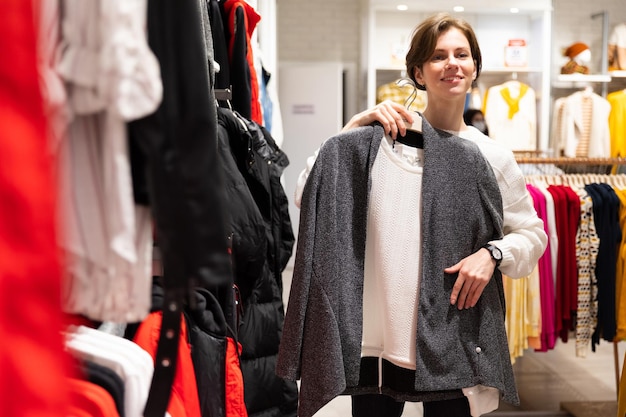 Foto der jungen attraktiven brünetten Frau mit kurzem Haarschnitt in einem weißen Pullover wählt stilvoll und