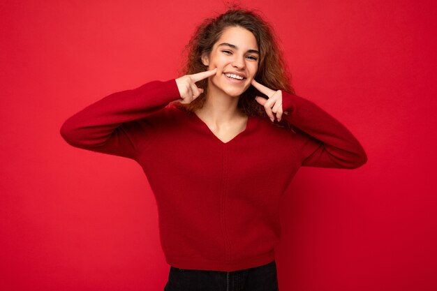 Foto der jungen positiven glücklich lächelnden attraktiven brünetten lockigen Frau mit aufrichtigen Gefühlen tragend