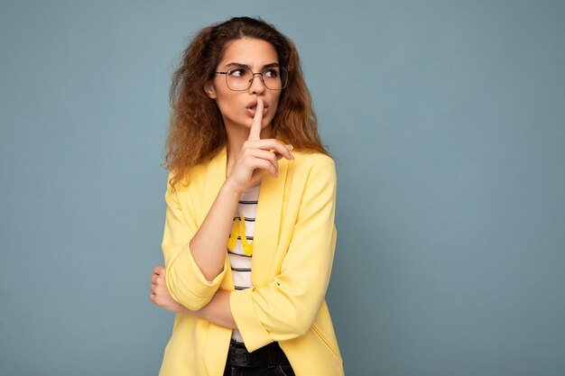 Foto der jungen, schönen, brünetten, lockigen Frau mit aufrichtigen Emotionen, die eine lässige gelbe Jacke trägt und