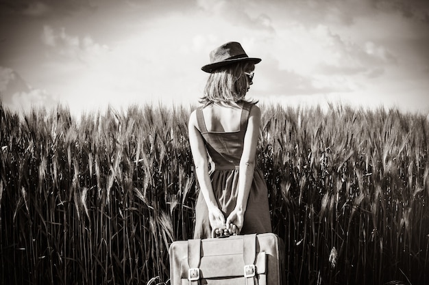 Foto der jungen schönen Frau mit Koffer im Feld. Bild im Schwarzweiss-Farbstil