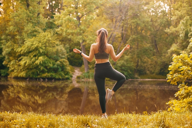 Foto der jungen schönen Sportfrau, die Yoga im Freien im Park nahe See ausübt