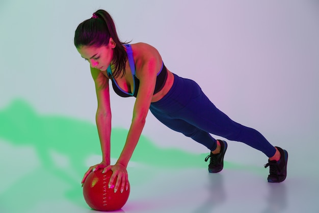 Foto der konzentrierten jungen Fitnessfrau, die mit LED-Blitzlichtern isoliert ist, macht Übungen mit Ball.