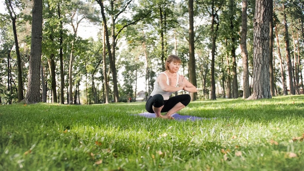 Foto der lächelnden Frau mittleren Alters, die Yoga Asana praktiziert. Persong, die in der Natur meditiert. Balance und Harmonie von Körper und Geist