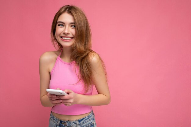 Foto der lächelnden gut aussehenden jungen blonden Frau, die rosa Top Poising lokalisiert auf Rosa trägt