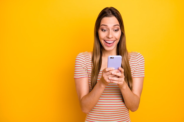 Foto der lustigen hübschen Dame halten Telefon Hände lesen gute Nachrichten überprüfen Anhänger Abonnenten Überraschung tragen lässig gestreiftes T-Shirt isoliert gelbe Farbe Wand