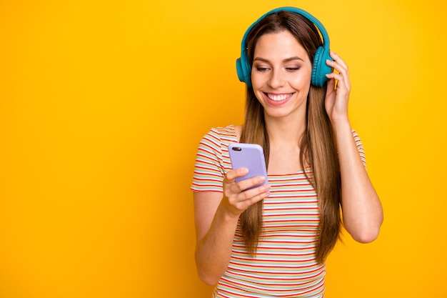 Foto der lustigen hübschen Dame halten Telefon hören Musik coole kabellose Kopfhörer, die Lied tragen lässig gestreiftes T-Shirt isolierte gelbe Farbwand einschalten