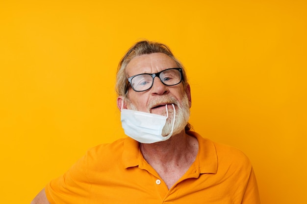 Foto der medizinischen Maske eines alten Mannes im Ruhestand in einem gelben Hemd, isolierter Hintergrund