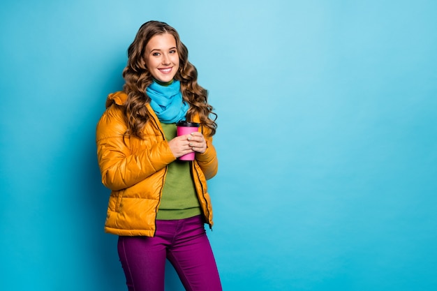 Foto der netten Dame halten heißes Papier Getränkebecher genießen Herbstwetter tragen lässig gelben Mantel Schal violette Hose grüner Pullover isoliert blaue Farbe Wand