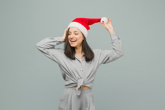 Foto der netten lächelnden Frau im Weihnachtshut sieht glücklich aus. Trägt graues Hemd, isolierten grauen Farbhintergrund.