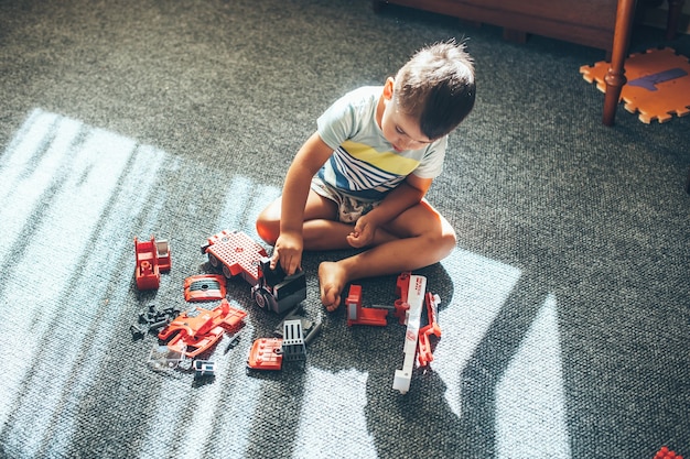 Foto der oberen Ansicht eines kaukasischen Jungen, der auf dem Boden mit Konstrukteurauto und Spielzeug spielt