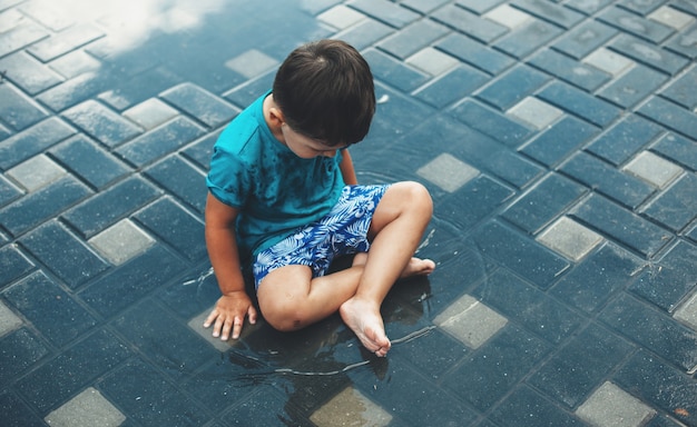 Foto der oberen Ansicht eines kaukasischen Jungen, der draußen im Wasser während der Sommerferien sitzt