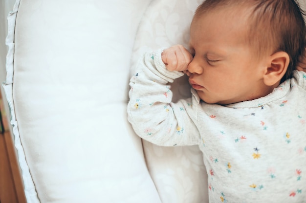 Foto der oberen Ansicht eines neugeborenen Babys, das im Safe auf einem weißen Bett schläft