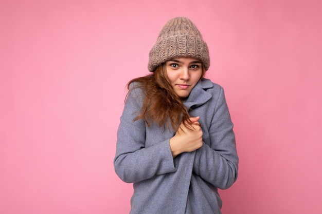 Foto foto der schönen attraktiven jungen brünetten frau, die über rosafarbener hintergrundwand isoliert ist und grau trägt