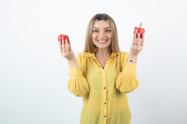 Foto der schönen blonden Frau, die rote Paprika hält und steht