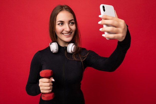 Foto der schönen glücklichen jungen brünetten Frau, die schwarze Sportkleidung weiße Kopfhörer trägt nad