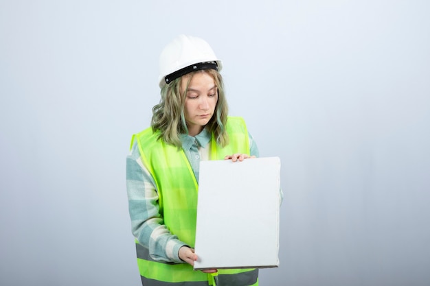 Foto der schönen Ingenieurin, die leere Leinwand über weißer Wand hält. Hochwertiges Foto