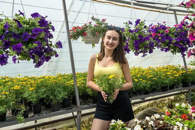 Foto der schönen jungen Frau, die zwischen Blumen in einem Gewächshaus aufwirft