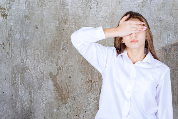 Foto der schönen langhaarigen Frau in der weißen Bluse, die ihre Augen bedeckt. Foto in hoher Qualität