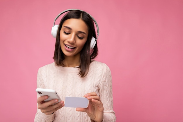 Foto der schönen positiven jungen brünetten Frau, die rosa lässigen Pullover lokalisiert über rosa trägt