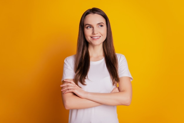 Foto der selbstbewussten Dame mit gefalteten Händen sieht leer aus, trägt weißes T-Shirt, das auf gelbem Hintergrund posiert