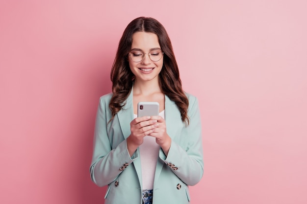 Foto der süßen Dame, die das Telefon hält und eine SMS schreibt, die auf rosafarbenem Hintergrund posiert
