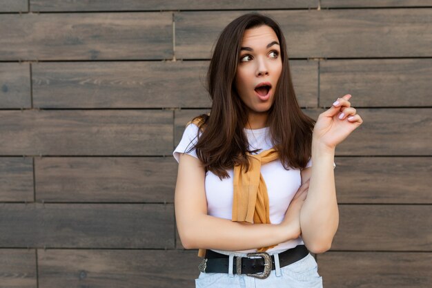 Foto der überraschten überraschten jungen Brunettefrau im modischen Outfit. Schöne attraktive weibliche Person, die draußen auf der Straße steht und eine Idee hat