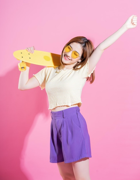 Foto des asiatischen Teenagermädchens mit Skateboard auf rosa Hintergrund