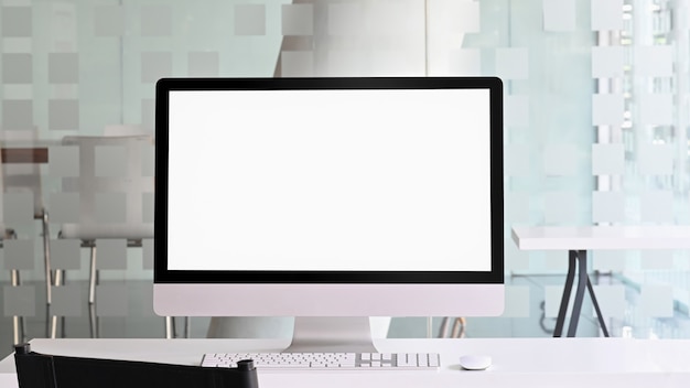 Foto des Computermonitors mit weißem leerem Bildschirm, der weißen Arbeitstisch mit drahtloser Maus und Tastatur über ordentlichem Büro setzt