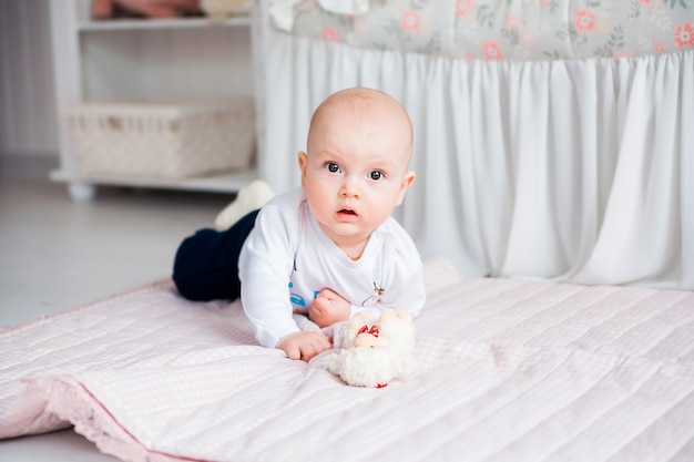 Foto des entzückenden Jungen, der auf dem Boden in ihrem Kinderzimmer liegt und mit Spielzeug spielt